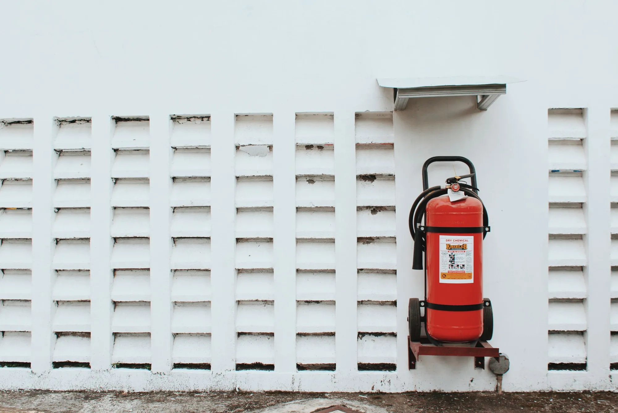 Extintor rojo instalado sobre una pared blanca de lamas, con su señalización